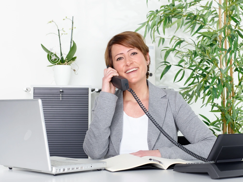 © Karin & Uwe Annas / Adobe Stock Geschäftsfrau mit Telefon und Computer am Schreibtisch.