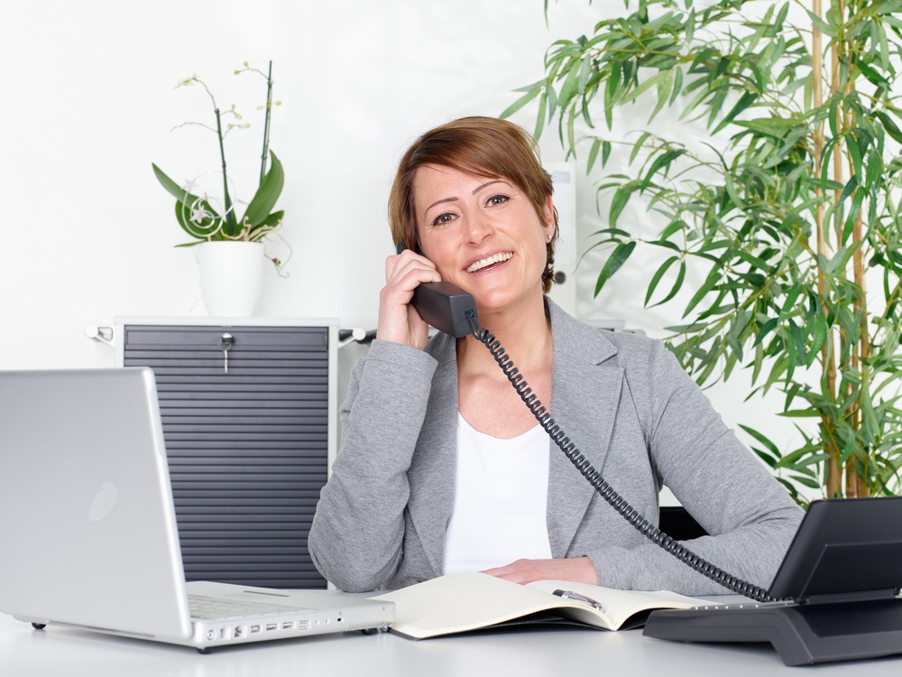 Geschäftsfrau mit Telefon und Computer am Schreibtisch.